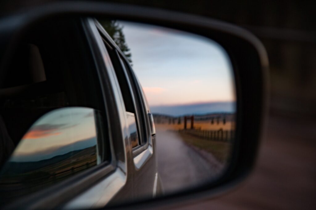 Photo of a car's side mirror, reflecting a receding road and mountains in the distance