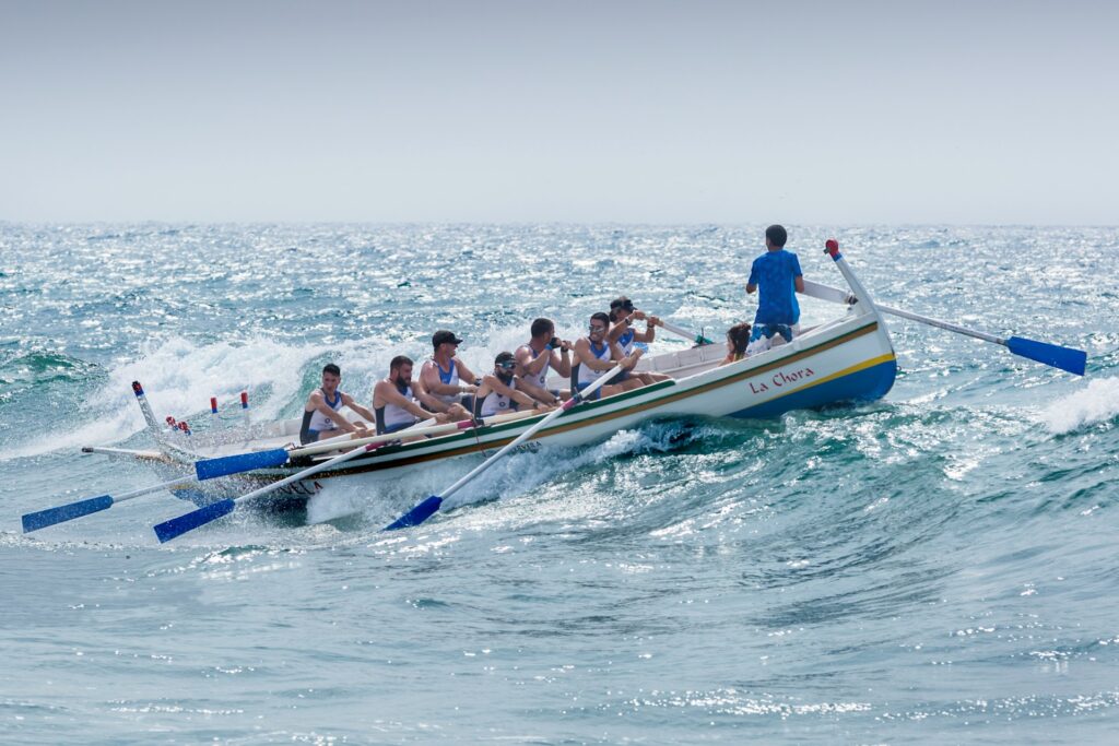 A group of men are rowing a large boat over waves in the open sea.