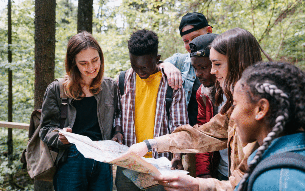 A group of 5 people in a forest, gathered together and looking at a map.