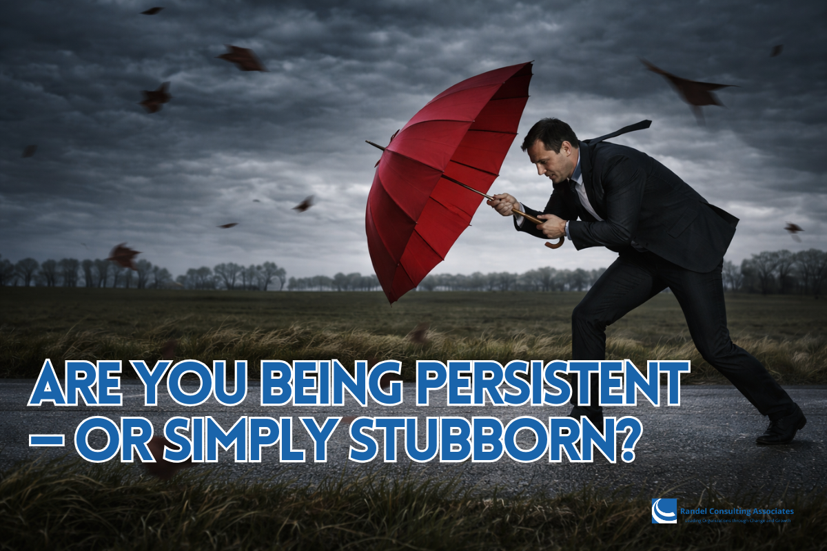 A businessman in a dark suit struggles forward along a rural road during a powerful windstorm, gripping a bright red umbrella that is pushed backward by strong gusts. Fallen leaves swirl through the air beneath a dark, stormy sky as he leans into the wind, bracing himself and pushing ahead despite the resistance.